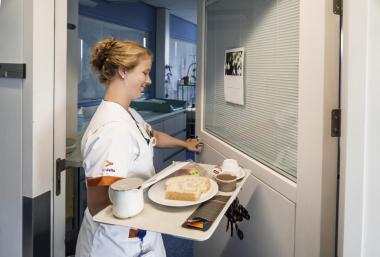 verpleegkundige die platteau met ontbijt binnenbrengt in kamer