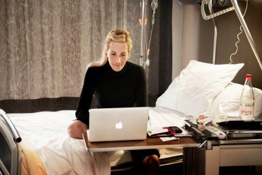 Een patiënte zit op bed met haar laptop