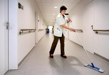 Een schoonmaakster aan het werk in een gang van het ziekenhuis